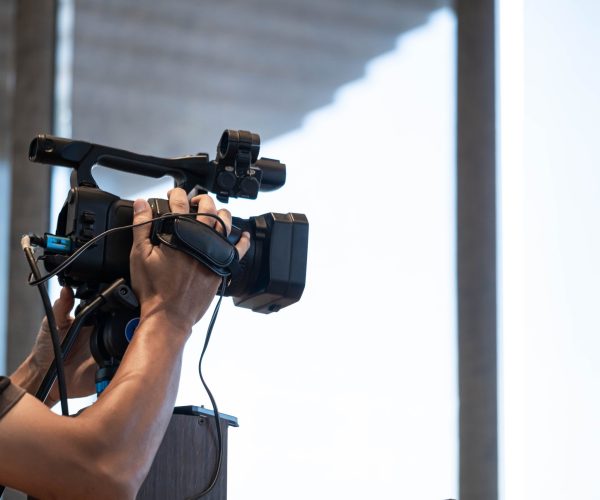 A person operating a professional video camera indoors, focusing on capturing footage.