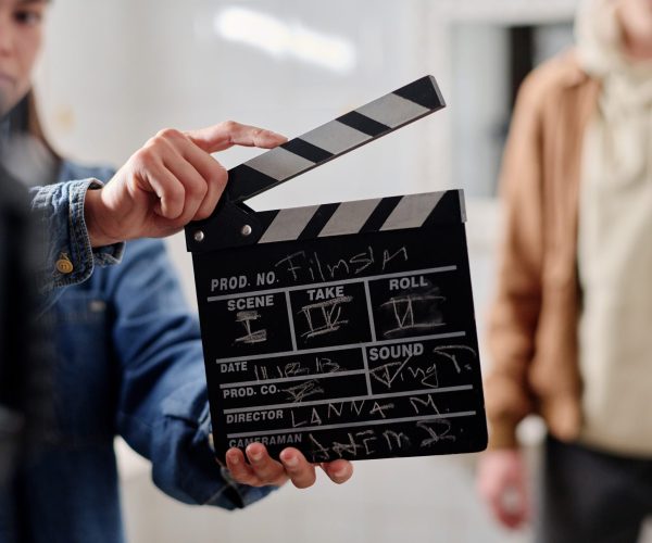 Crew member holding film clapper while preparing for a movie scene on a film set. Blurred background includes another crew member standing, adding depth to film production scene