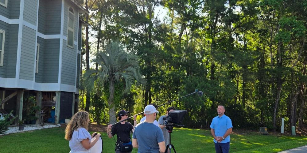 Tampa Bay business owner reviewing a video production company evaluation checklist with Benjamin Tone of Tone Production — five commercially objective criteria including commercial brief process, crew architecture, 8K RAW cinema technical ceiling, DaVinci Resolve post-production, and AI-generated semantic delivery laid out on a production planning document at a Tampa Bay brand video agency selection meeting